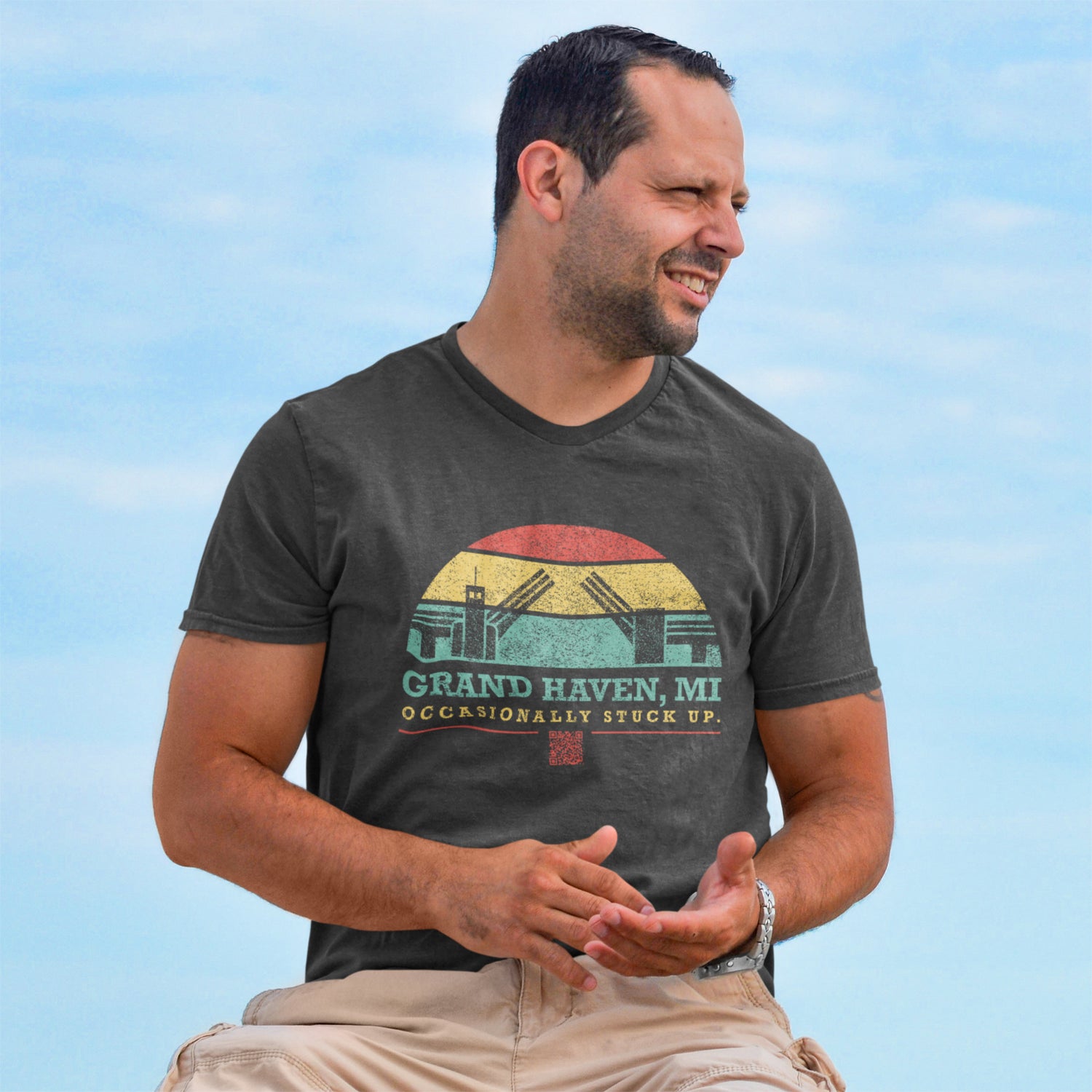 Man wearing occasionally stuck up tee on beach with blue sky in background.