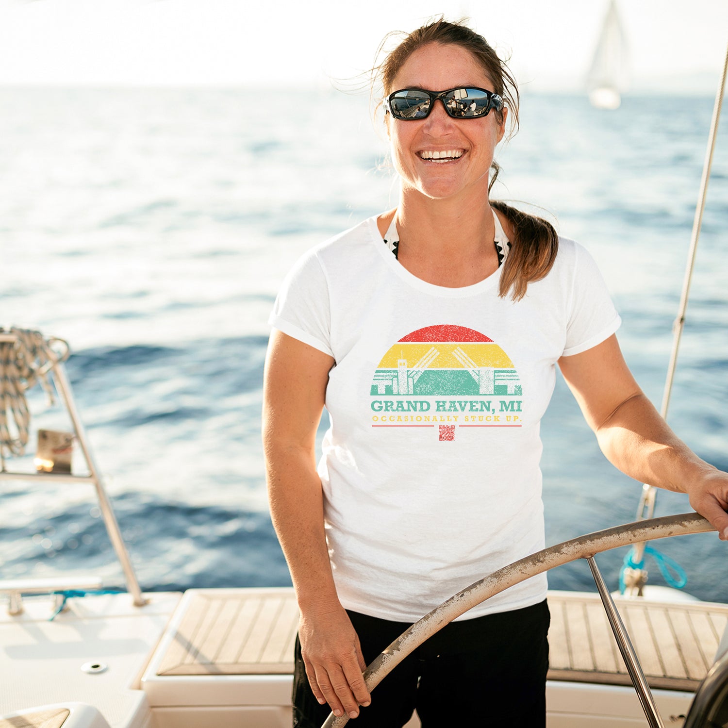 Middle aged woman at the wheel of a boat on the water in Grand Haven, wearing an "occasionally stuck up" t shirt